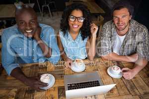 Happy friends having coffee with laptop on table in cafe