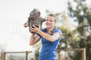 Smiling woman carrying heavy wooden logs during obstacle course