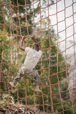Military soldier climbing net during obstacle course