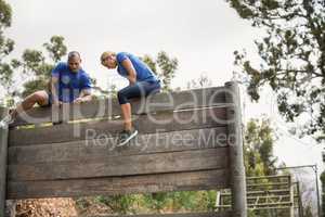 Fit man and woman climbing over wooden wall during obstacle course