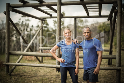 Fit woman and man standing against monkey bars during obstacle course