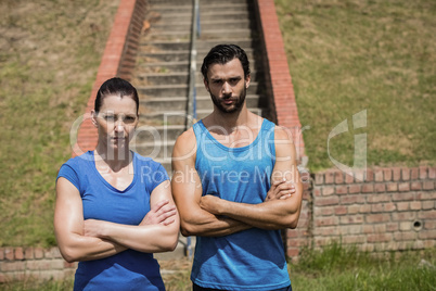 Portrait of fit man and woman standing with arms crossed against staircase