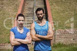 Portrait of fit man and woman standing with arms crossed against staircase