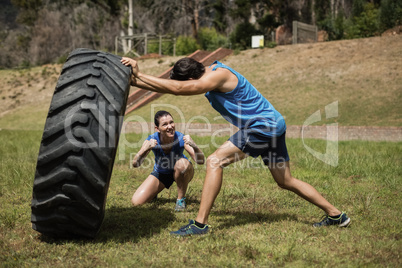 Fit man flipping a tire while trainer cheering during obstacle course