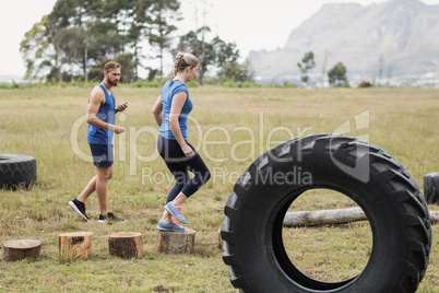 Fit woman running on wooden logs while trainer measuring time