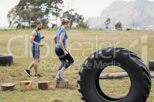 Fit woman running on wooden logs while trainer measuring time