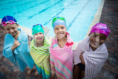 Little swimmers wrapped in towels standing at poolside
