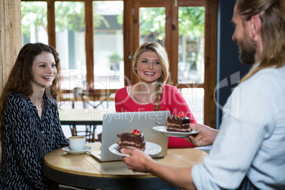 Male barista serving dessert to customers in coffee shop