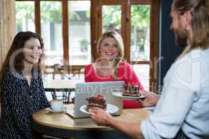 Male barista serving dessert to customers in coffee shop