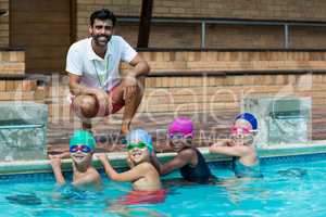 Happy male trainer with little swimmers at poolside