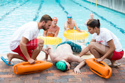 Male and female lifeguards helping unconscious man