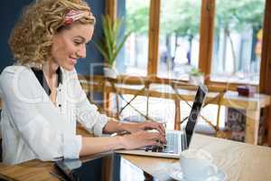 Smiling woman using laptop at table in cafeteria