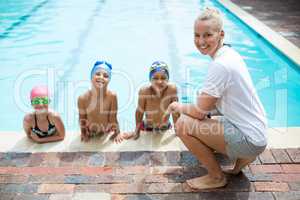 Female swimming trainer teaching students at pool side