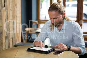 Man using digital tablet at wooden table in cafe