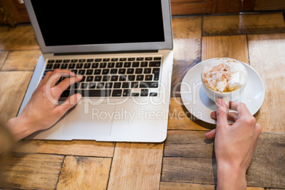 Woman holding coffee cup while using laptop in cafe