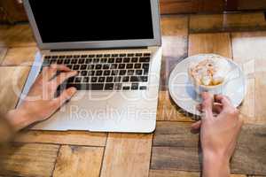 Woman holding coffee cup while using laptop in cafe