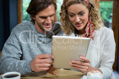 Loving couple using tablet computer at table in cafeteria