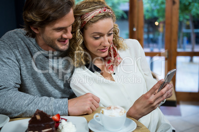 Loving couple using smart phone at table in cafeteria