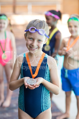 Happy little girl showing medal at poolside