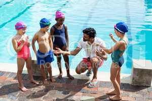 Male trainer assisting children at poolside