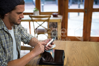 Young man using smart phone at table in coffee shop
