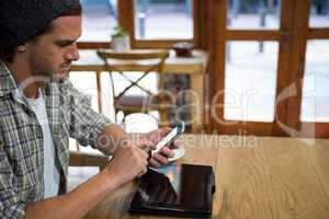 Young man using smart phone at table in coffee shop