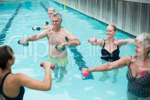 Senior swimmers and instructor lifting dumbbells in swimming pool