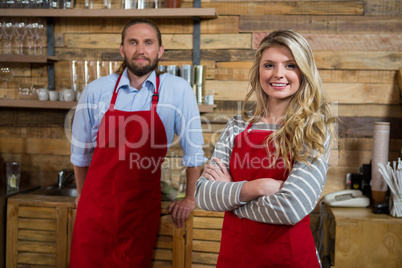 Smiling female barista with male colleague in coffee shop