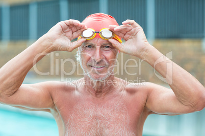 Senior man holding swimming goggles at poolside