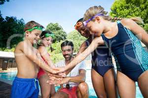 Instructor and children stacking hands at poolside