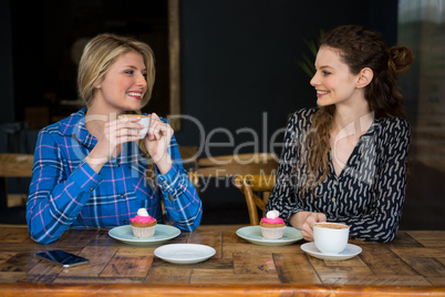 Beautiful female friends having coffee while talking in cafeteria