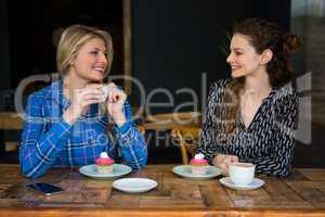 Beautiful female friends having coffee while talking in cafeteria