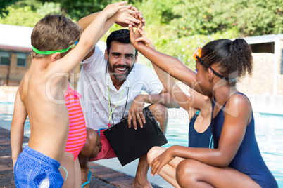 Children stacking hands with trainer at poolside