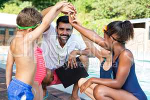 Children stacking hands with trainer at poolside