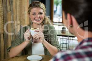 Smiling woman holding coffee cup while looking at man in cafe