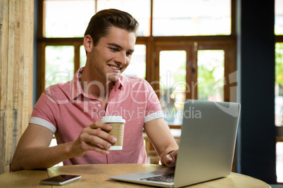 Smiling man using laptop while having coffee in cafe