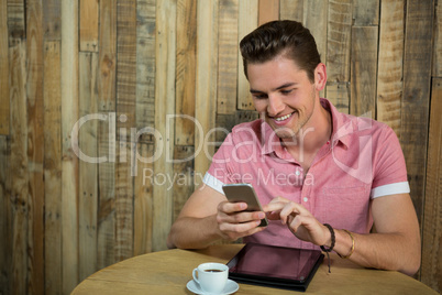 Smiling man using smart phone at table in coffee shop