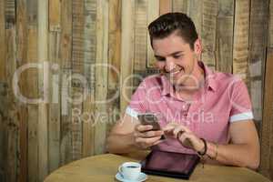 Smiling man using smart phone at table in coffee shop