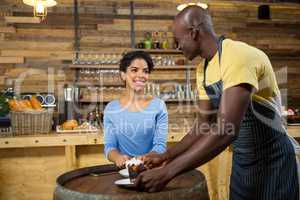 Young barista serving coffee to woman at table