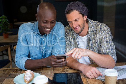 Happy male friends using mobile phone in coffee house