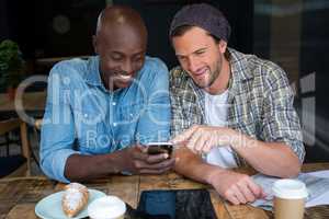 Happy male friends using mobile phone in coffee house