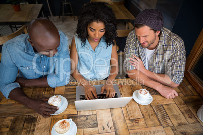 Friends using laptop at wooden table in coffee shop