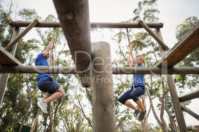 Fit man and woman climbing rope during obstacle course