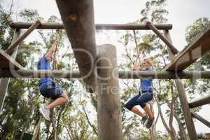 Fit man and woman climbing rope during obstacle course