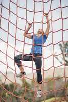 Fit woman climbing a net during obstacle course