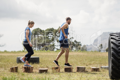 Fit woman and man running on wooden logs during obstacle course