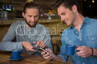 Happy male friends using smart phone in coffee house