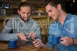 Happy male friends using smart phone in coffee house