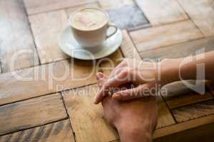 Couple holding hands with coffee cup on table in cafe