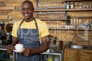 Smiling male barista holding coffee cup in cafe